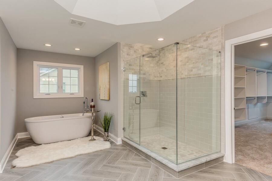 Modern bathroom with freestanding tub, glass shower, and herringbone tile floor leading to walk-in closet