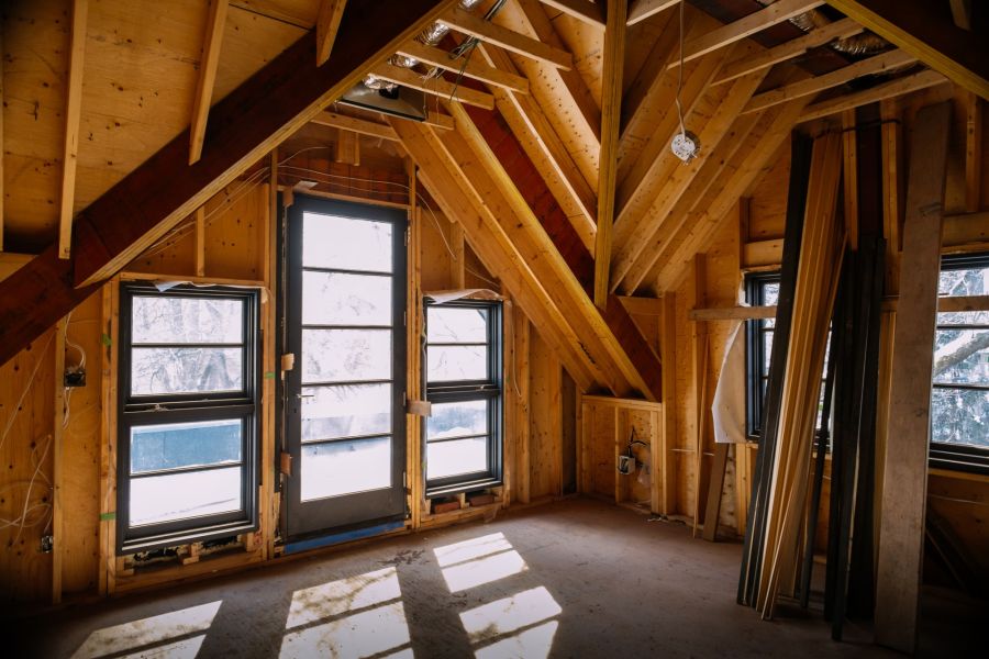 Unfinished home addition interior with exposed wood framing, windows, and a door
